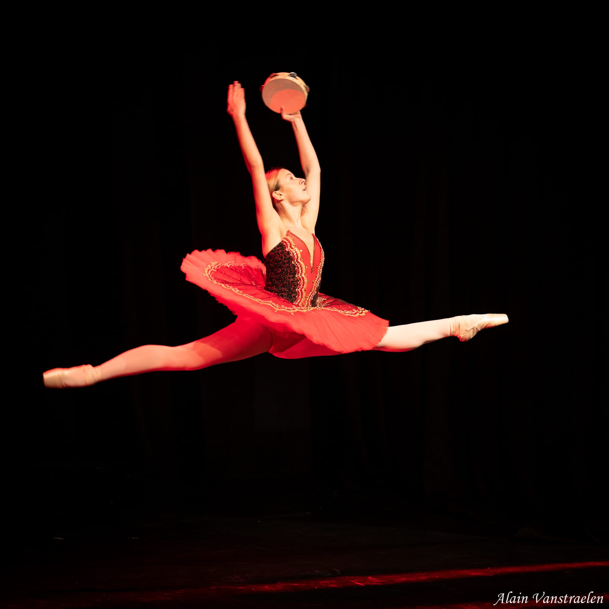 Danseuse en tutu rouge et or, grand jeté avec un tambourin levé
