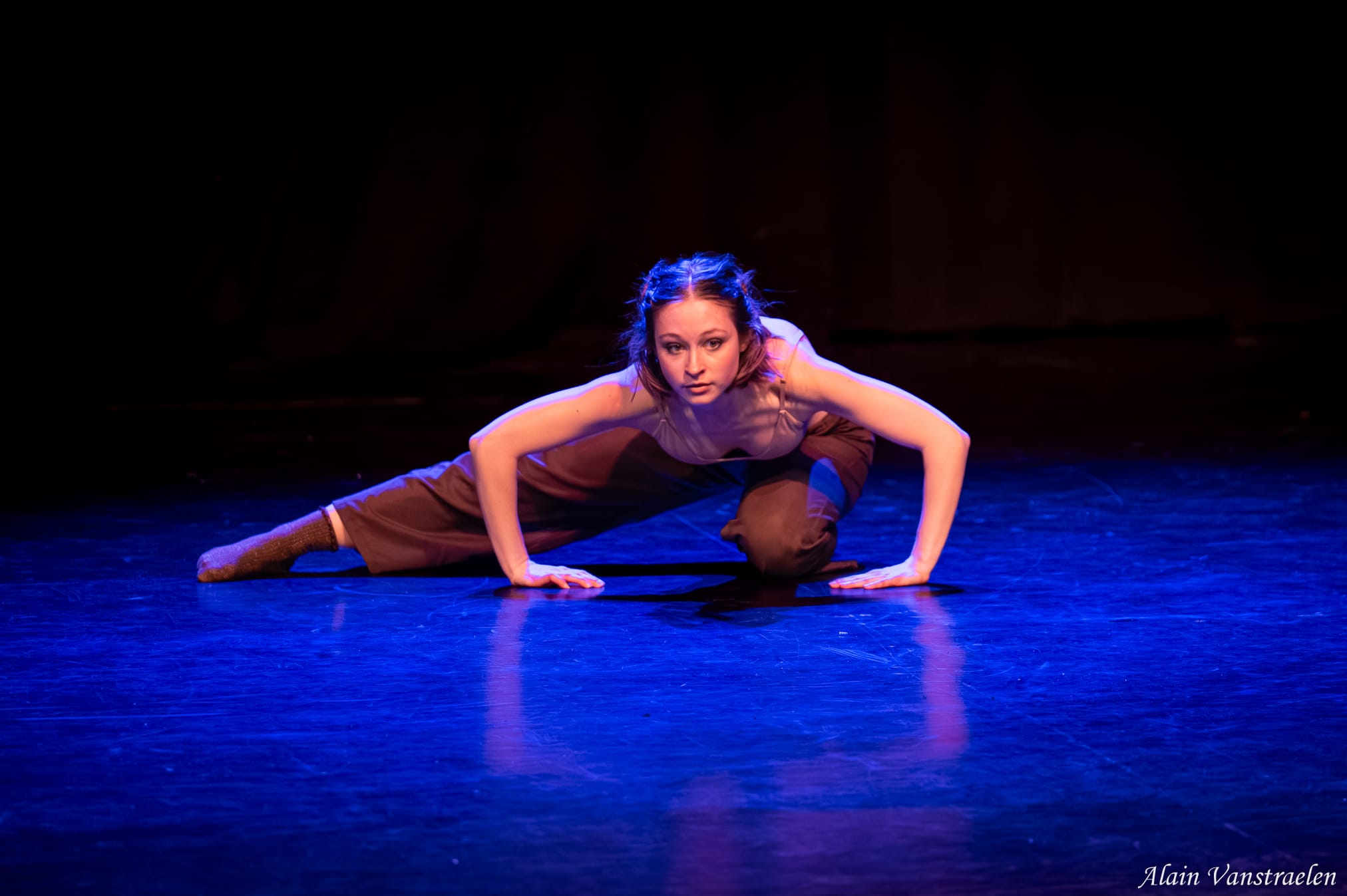 Danseuse contemporaine au sol, appuyée sur les mains, lumière bleue