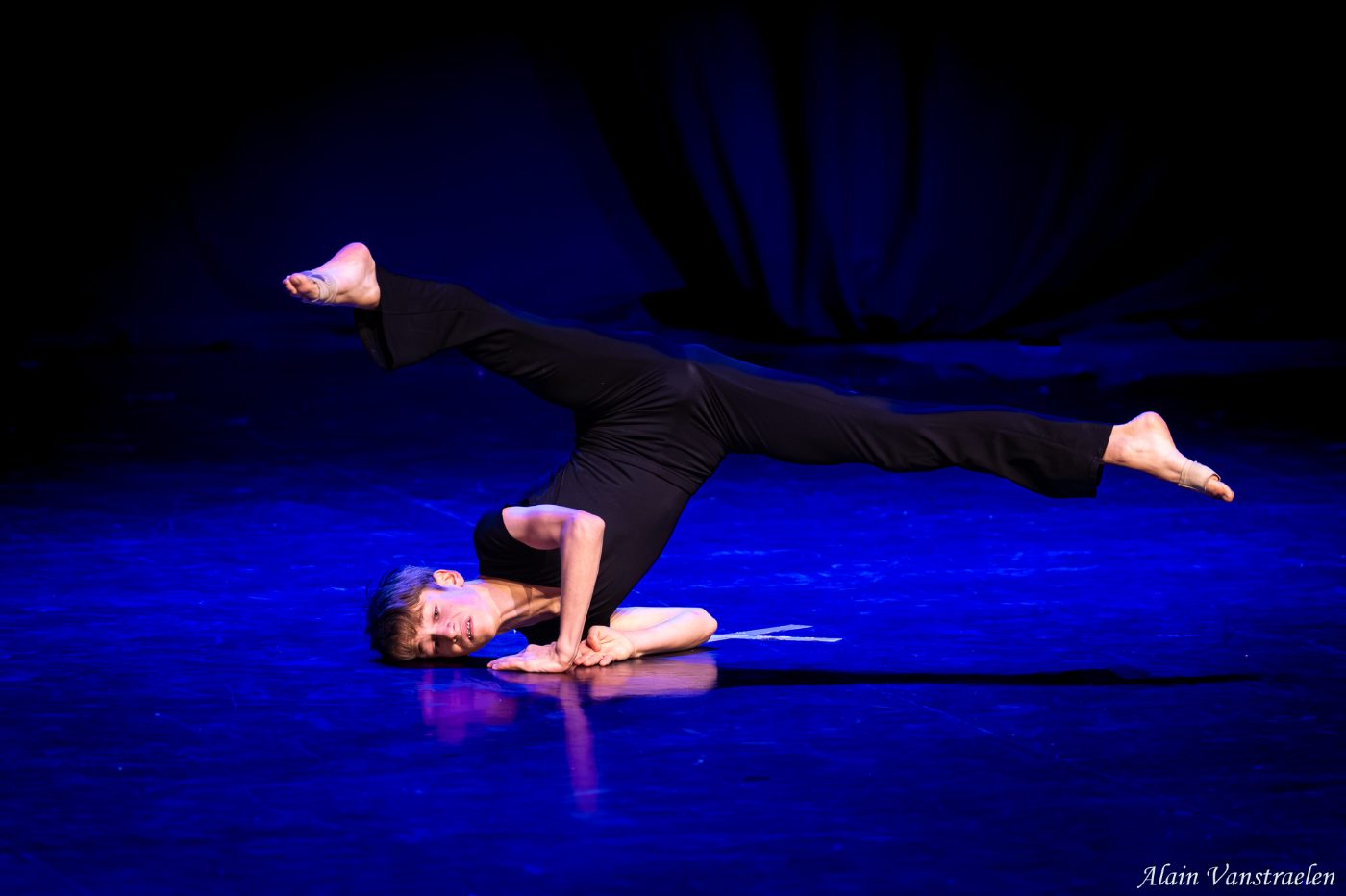 Danseur en noir en équilibre sur les avant-bras, jambes tendues à l'horizontale, lumière bleue