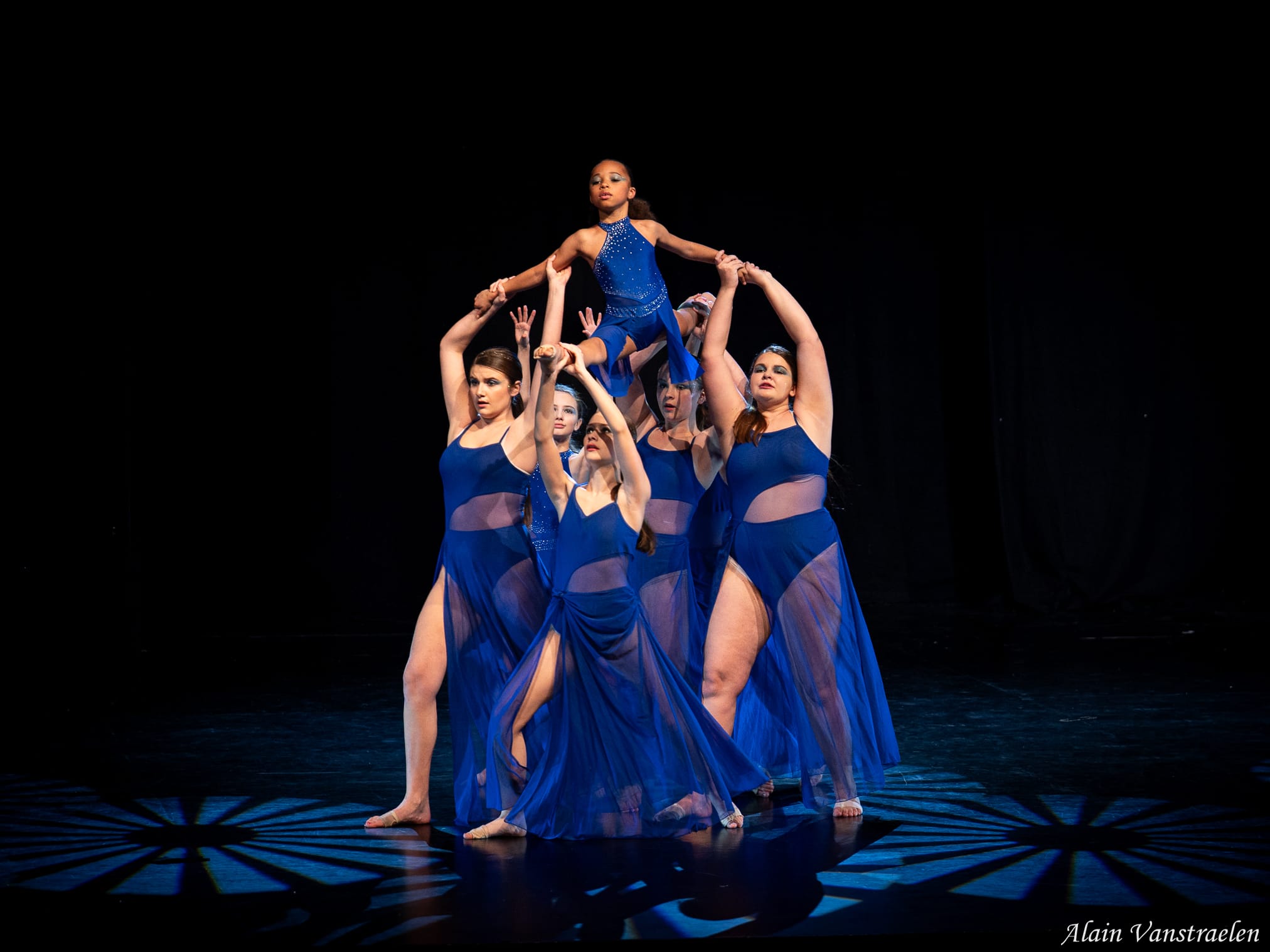 Groupe en robes bleues portant une jeune danseuse au sommet d'une pyramide