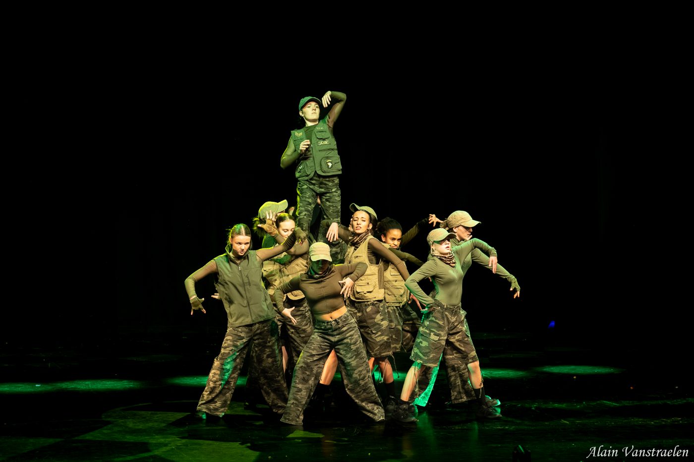 Groupe de danseurs en tenue camouflage formés en pyramide, lumière verte