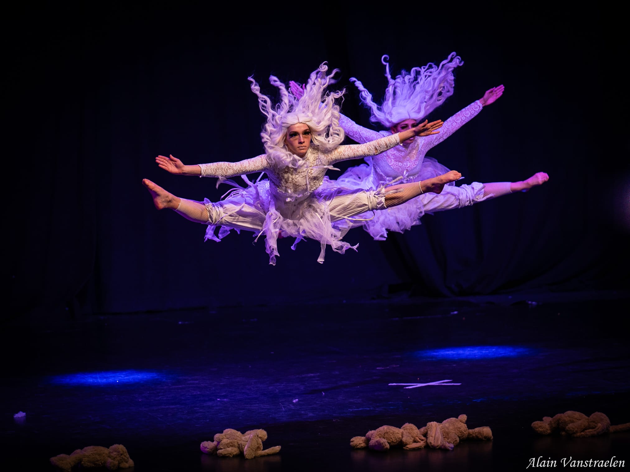 Deux danseuses en costumes blancs sautées en grand écart au-dessus de la scène, lumière violette